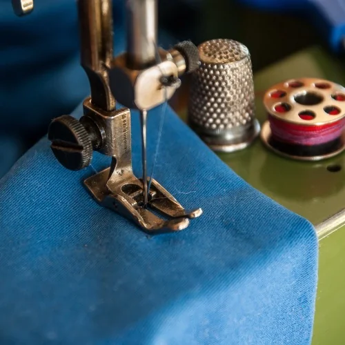 Sewing-machine needle stitching blue fabric beside a thimble