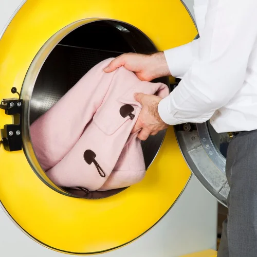 Hands placing a pink coat into a garment-cleaning machine
